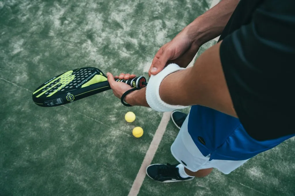 Raquette de padel tenue au-dessus du court près de deux balles
